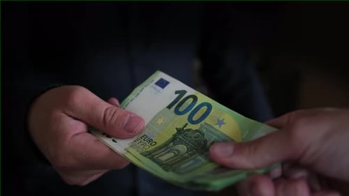 Man's hand holds out stack of one hundred euros bills to another person, close-up