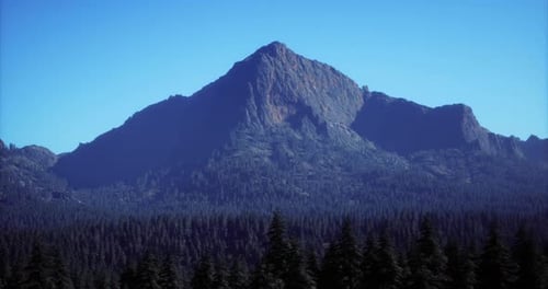 Majestic Mountain Peak Rising Above Dense Forest Under Clear Blue Sky
