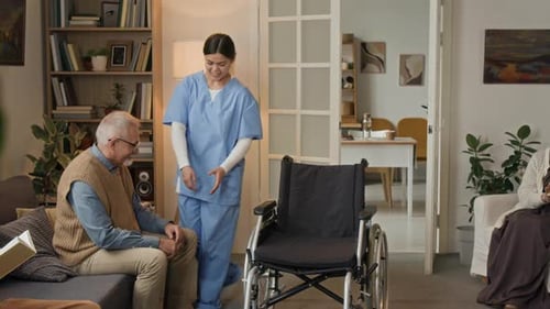 Caregiver Helping Senior Man into Wheelchair in Home