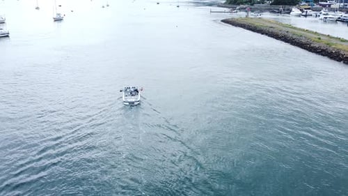 Following motor boat vessel aerial view navigating quiet river Conwy harbour marina seaside town