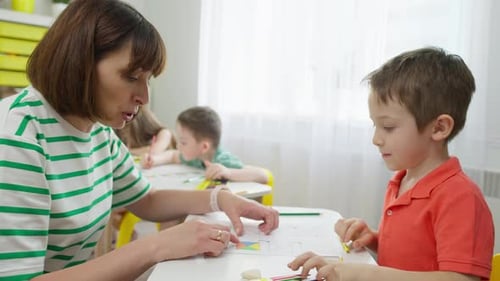 Teacher Helping Boy with Art Project in Classroom