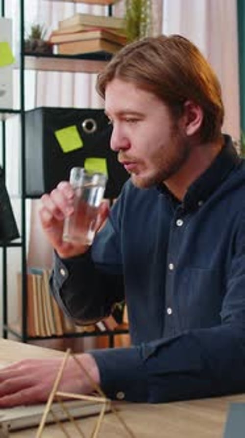 Businessman Sitting at Workplace Desk Drinking Water While Working with Laptop in Home Office