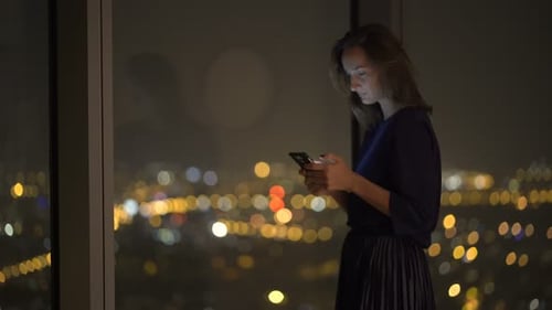 Woman Using Smartphone Near Window at Night