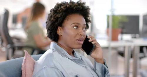 Happy african american casual businesswoman talking on smartphone in office, slow motion