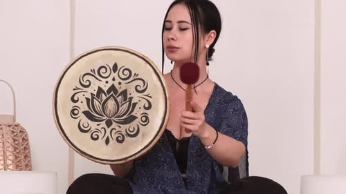 Woman Plays Round Drum Indoors with Wooden Stick