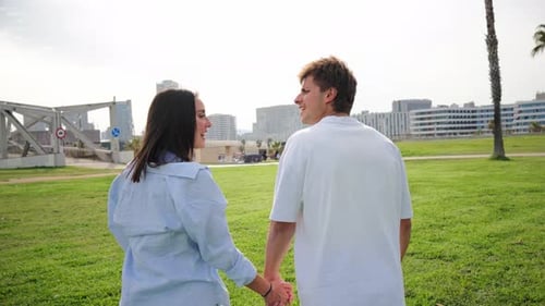 Joyful Couple Holding Hands While Walking Together in a Beautiful Park Filled with Lush Greenery