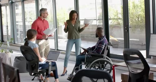 Team of diverse male and female colleagues discussing together at office, man in wheelchair