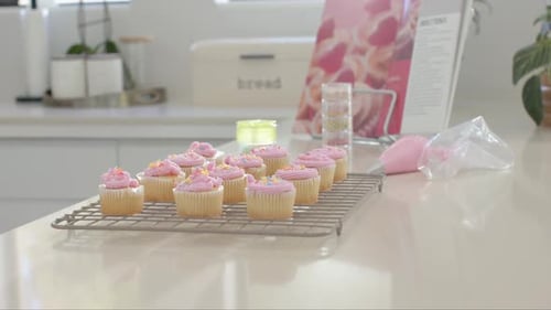 La cámara se está retirando, mostrando los cupcakes en la rejilla de refrigeración sobre la parte superior brillante, mostrando la decoración terminada
