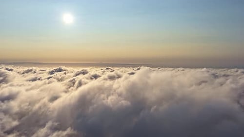 Aerial pullback flying above vast sea of clouds with bright sun and warm golden horizon