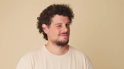 Nahaufnahme eines Mannes, der im Studio auf beigem Hintergrund in die Kamera blickt, mit blinzelndem Auge