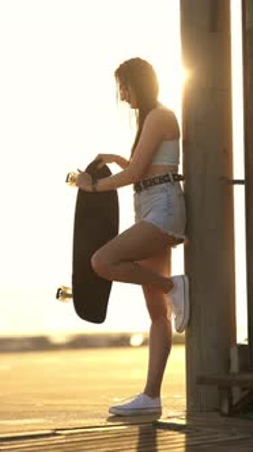 Stylish Woman With Skateboard on Beach at Sunset