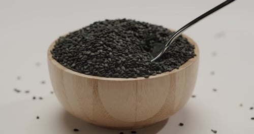 Spoon scooping black sesame seeds from wooden bowl