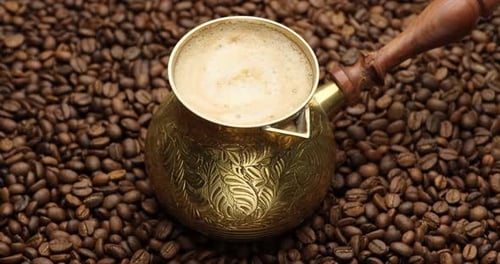Steel Cezve Surrounded By Roasted Coffee Beans on a Rotating Background