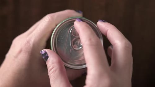 Female hand opening beer can on wooden table in restaurant.Close up top down shot.