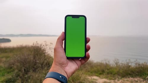 Person Hands Hold Vertical Mobile Phone with Green Screen Against Background Ocean and Clouds Sky
