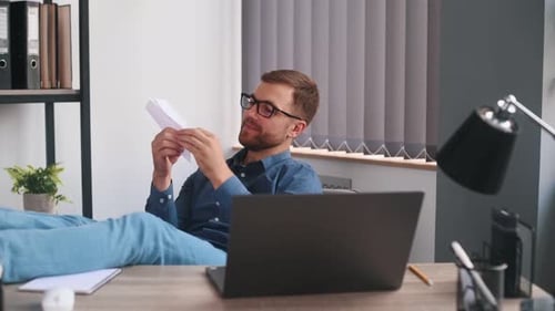 Papierflugzeug werfen. Männlicher Freelancer sitzt mit Laptop am Tisch und hat Spaß
.