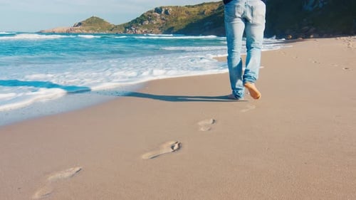 Man in blue jeans walks barefoot on the sandy beach
