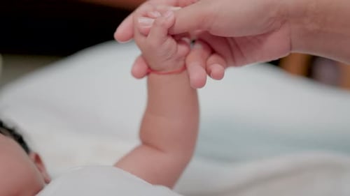 Close-up of a newborn baby playing with its mother's hands and fingers while lying on its back