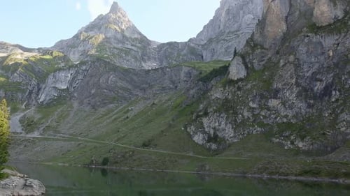 Eroded rocks of Alps Mountain casting shadow on Bannalp Lake quiet water