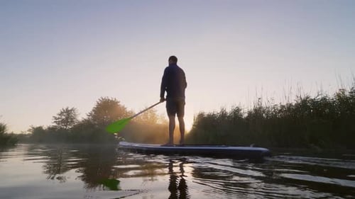 People Riding Paddleboards in River at Sunrise