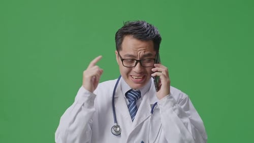 Asiatischer männlicher Arzt mit Stethoskop schreit auf dem Smartphone, während er auf einem Greenscreen steht