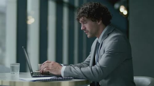 Focused Businessman Typing on Laptop at Table in Restaurant