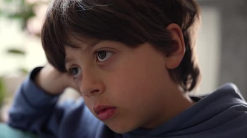 Pensive boy resting head on hand with absorbed expression during quiet moment of contemplation