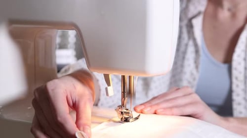 Woman sewing fabric with professional machine in workshop, closeup