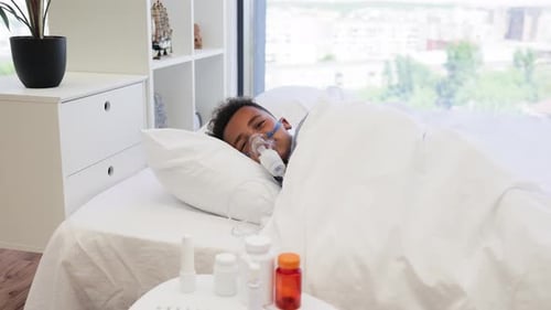 Garçon africain utilisant un nébuliseur pour un traitement respiratoire à la maison au lit
