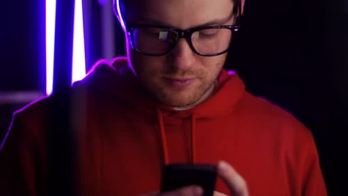 Young man texting on smartphone in dark room with ultra violet neon lights