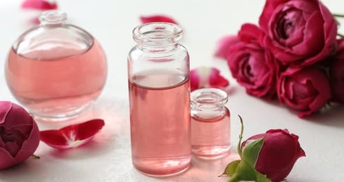 Rosenblätter, die auf den weißen Tisch fallen, mit offenen Parfümflaschen mit ätherischen Ölen, Nahaufnahme