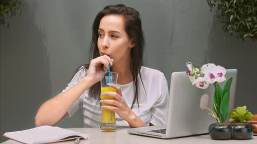 Woman Drinking Juice at Table with Laptop