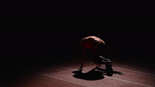 Sprinter Prepares at Starting Blocks at Night