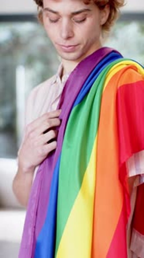 Young Adult Smiles Holding Rainbow Flag Indoors