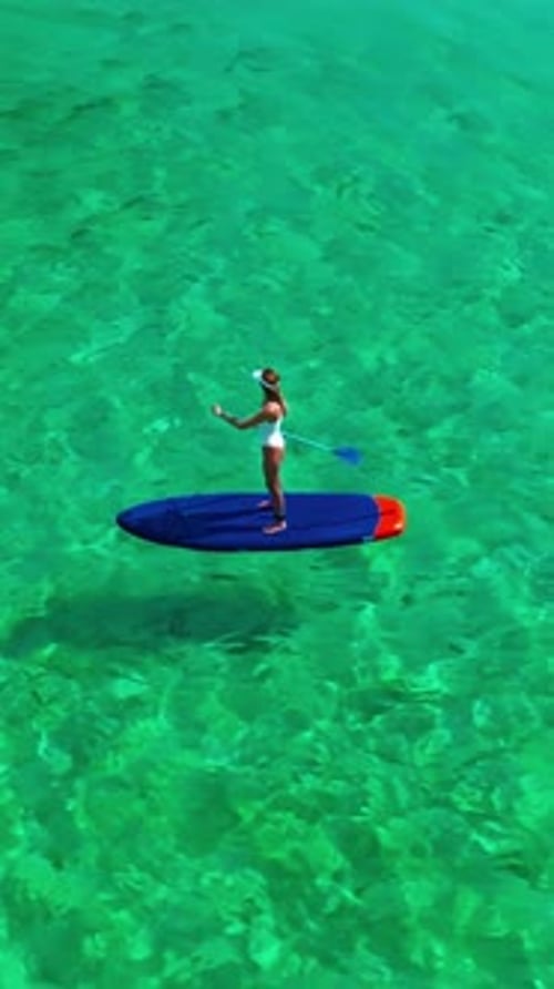 Aerial View of Woman in White Swimsuite Standing on Sup Board with Paddle on Crystal Turquoise Water
