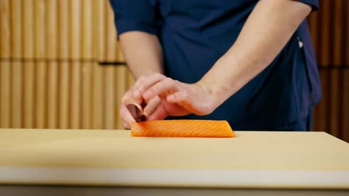 Close Up in a Japanese Restaurant Chef in a Blue Uniform Cuts Fish for Sushi Into Slices on a Yellow