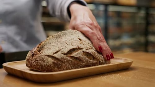 Nahaufnahme, Bäckerei - Bäckerin schneidet frisch gebackenes Schwarzbrot