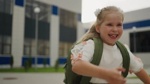 Schulanfang, Porträt eines rennenden Schulmädchens mit Rucksack auf dem Schulhof Glückliche Kindheitsmomente