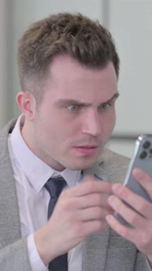 Portrait of Young Businessman Reacting to Loss on Smartphone, vertical video