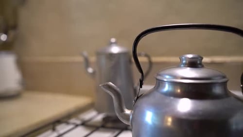 Boiling kettle on cooker grill with steam exiting from spout. Handheld
