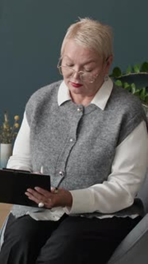 Vertical Portrait of Mature Female Psychologist Taking Notes in Office