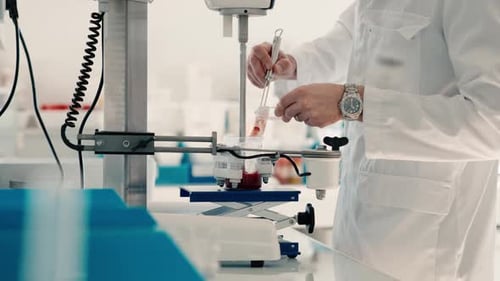Personne vêtue de vêtements de laboratoire blancs ajoutant un colorant. Cette procédure méthodique est un coin