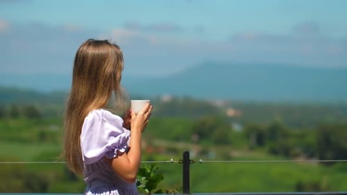 Young Woman with Long Blonde Hair Standing on Terrace and Holding Cup