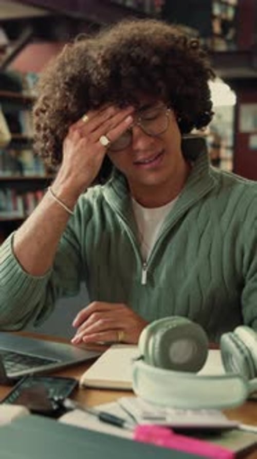 Frustrated, man and student with headache in library for overworked strain or studying
