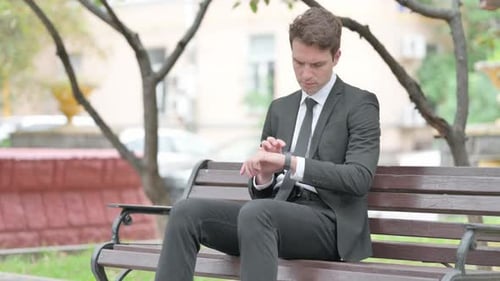 Businessman Looks at Watch While Sitting on Bench