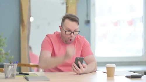 Man Celebrates Success While Using Smartphone Indoors