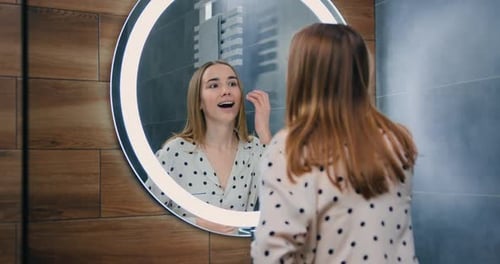 Hermosa jovencita en el espejo en el baño de su casa. Rutina femenina, facial, salud, cuidado corporal, vida