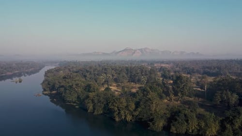 A serene river winding through a lush forest with distant mountains in the background, aerial view