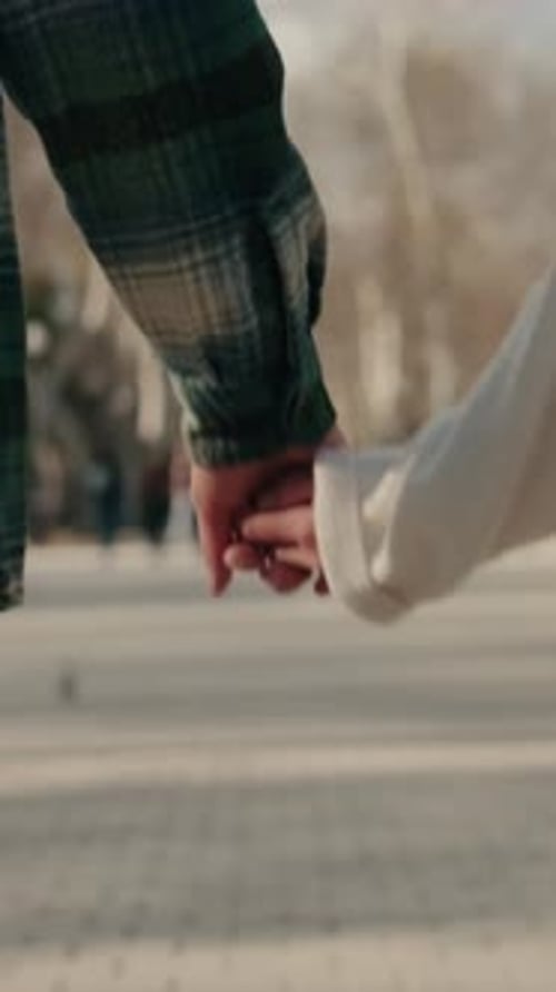 Close up of hands of young couple holding hands and walking down street