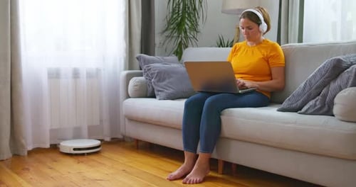 Woman Working on Laptop with Robot Vacuum